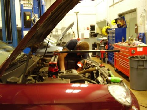 1997 Ford Taurus - A mechanic is focused on repairing the engine of a red vehicle in a workshop setting that appears to be a repair shop.
