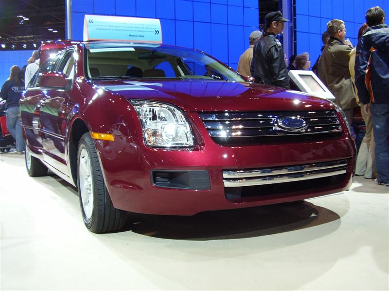 Red Ford sedan with chrome grille and headlights, seen at an auto show