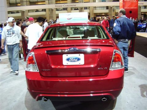 1997 Ford Taurus - A red Ford Fusion is displayed at an auto show, with people milling around.