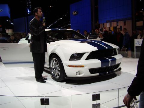 1997 Ford Taurus - A white Ford Mustang GT500 with blue racing stripes is presented at an auto show.