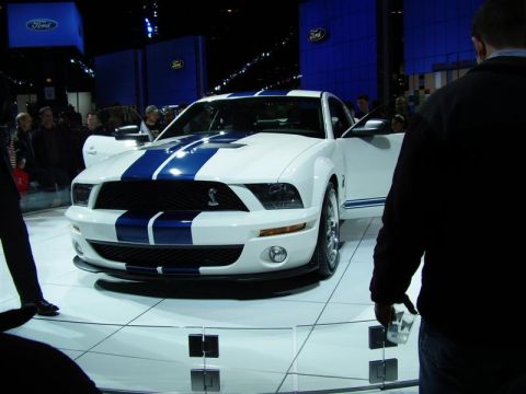1997 Ford Taurus - A white 2007 Ford Mustang Shelby GT500 with blue racing stripes is showcased at an auto show.