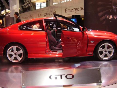 1997 Ford Taurus - A red Pontiac GTO is displayed with its doors open, showing the interior and a prominent GTO badge on a stand.