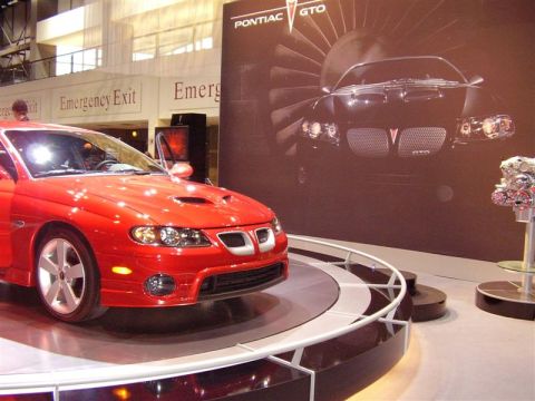 1997 Ford Taurus - A red Pontiac GTO is displayed at an auto show with promotional graphics and an engine exhibit.