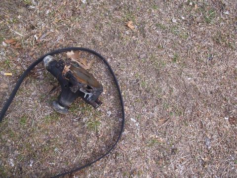 1989 Ford Bronco - A damaged water pump with a black hose rests on the ground.