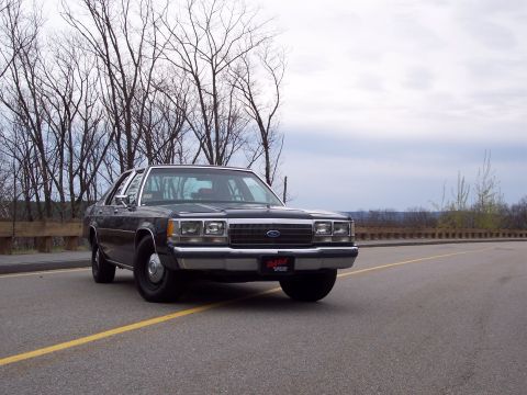 2001 Ford Crown Victoria - Low 3/4-front view of a black Ford Crown Victoria sedan parked on a roadside pull-off, wearing black steel wheels with center caps and a re…