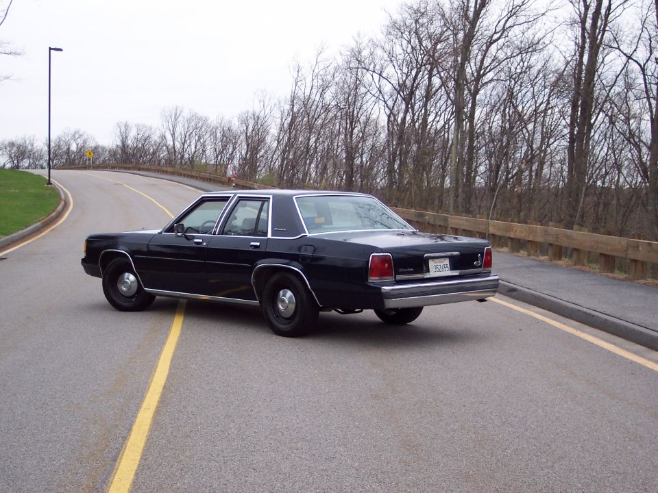 Black 2001 Ford Crown Victoria sedan, 3q-front view, on a road with a wooden fence