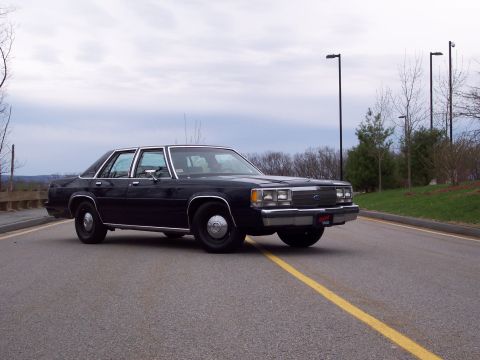 2001 Ford Crown Victoria - Black sedan with chrome trim and steel wheels parked on a road.