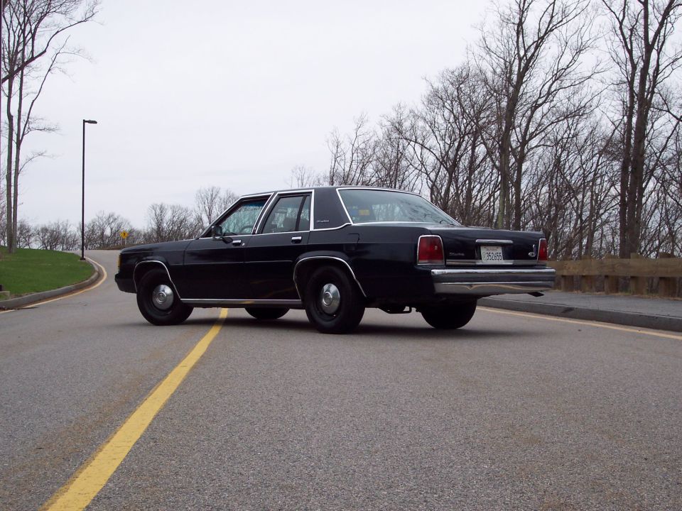 Black sedan from rear, driving on a road with a yellow line