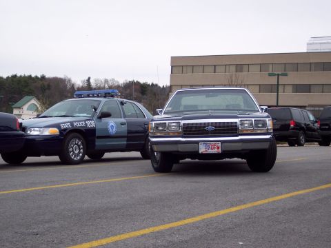 2001 Ford Crown Victoria - Two police vehicles are parked in a lot, one in the foreground and another to the left.