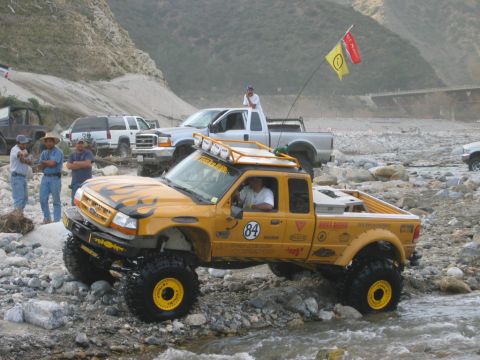 1985 Ford Bronco - Multiple off-road vehicles navigate a rocky, watery terrain, with a yellow Ford Ranger in the foreground.