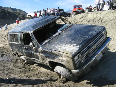 1985 Ford Bronco - Off-road enthusiasts watch as a mud-covered Chevrolet K5 Blazer gets stuck in the sand and dirt.