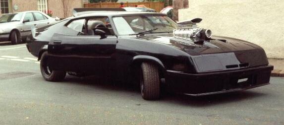 black coupe with supercharger sticking out of hood, parked on street. Another car in background