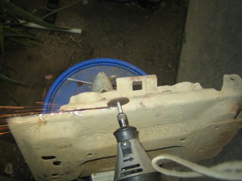 1990 Ford Bronco - handheld rotary tool grinds a weld on a metal bracket held over a blue bucket, throwing a spray of sparks.