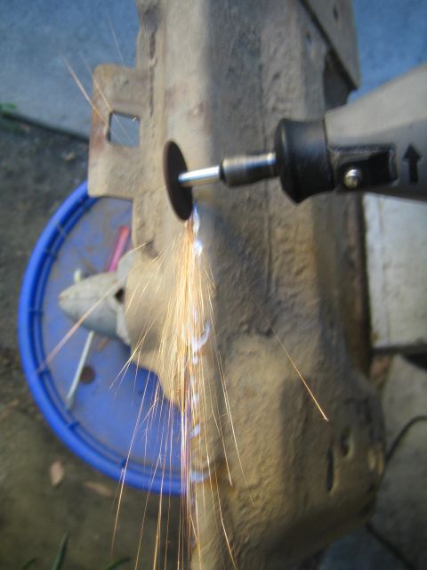 1990 Ford Bronco - handheld rotary tool cuts into a rusty metal bracket, sending a stream of sparks downward over a blue bucket.