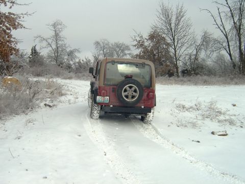 1998 Jeep TJ - A red Jeep Wrangler navigates a snow-covered path with trees in the background.