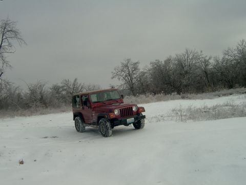 1998 Jeep TJ - A red Jeep Wrangler drives through a snowy landscape under an overcast sky.