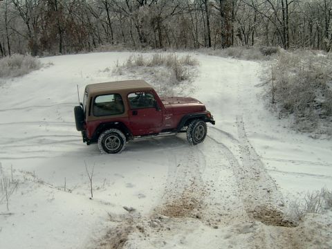 1998 Jeep TJ - Red 1998 Jeep TJ navigates a snowy trail in a wooded area.