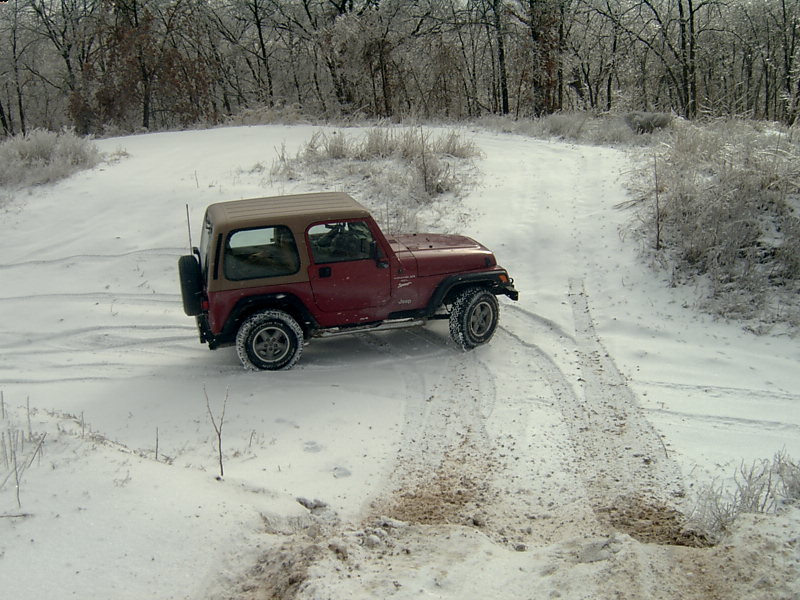 1998 Jeep TJ driving on a snow-covered dirt road with trees in the background