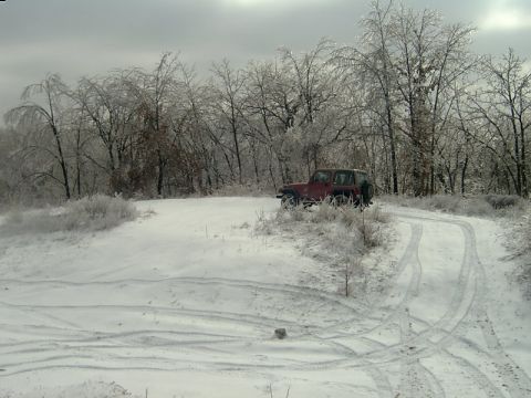 1998 Jeep TJ - A red Jeep navigates a snow-covered path through a winter landscape with ice-laden trees.