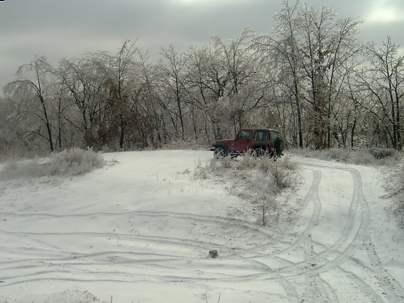Red Jeep Wrangler on a snowy, icy road with trees covered in ice