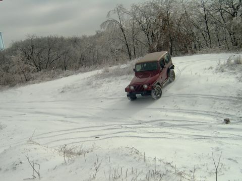 1998 Jeep TJ - A red Jeep Wrangler navigates a snowy, icy landscape with trees in the background.