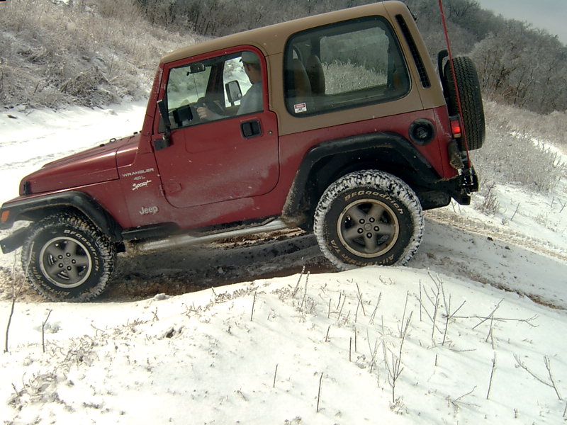 Red 1998 Jeep TJ driving on a snowy trail