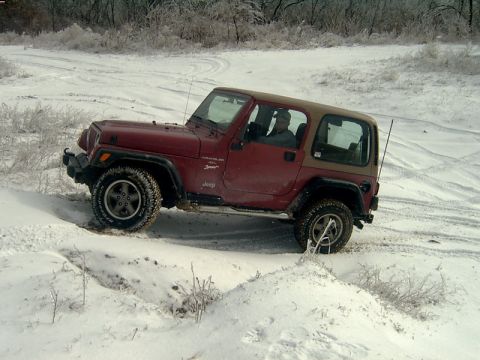 1998 Jeep TJ - A red Jeep Wrangler navigates a snowy path with trees in the background.