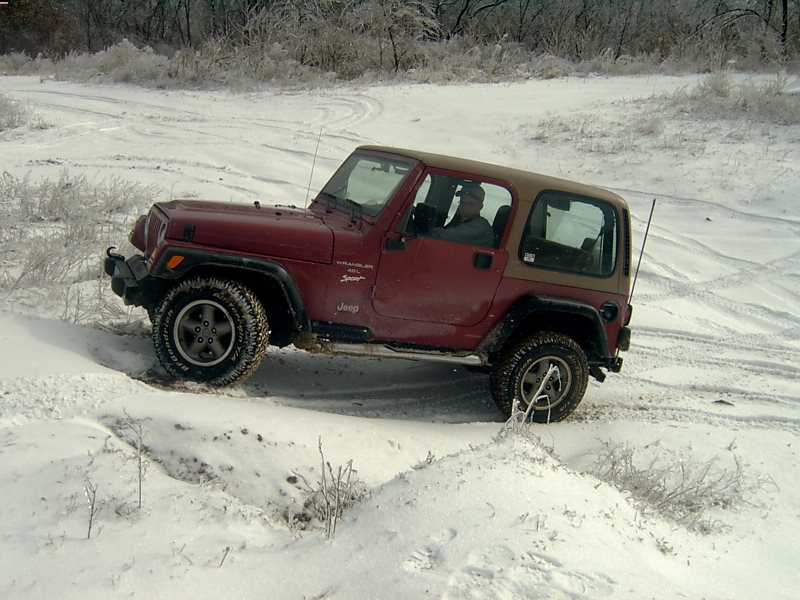 Red Jeep Wrangler driving on a snowy trail. The Jeep has a tan soft top