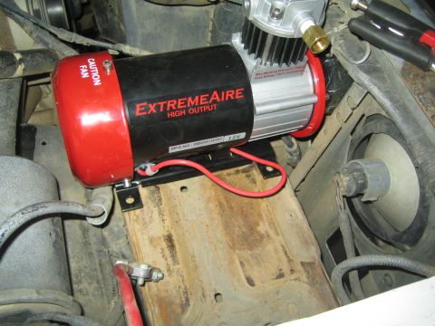 1990 Ford Bronco - red and black ExtremeAire High Output 12V air compressor mounted on a bracket inside a vehicle engine bay.
