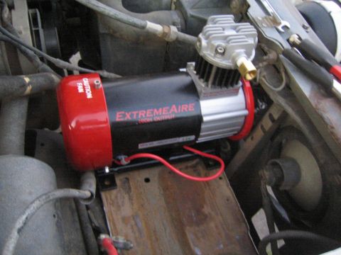 1990 Ford Bronco - red and black ExtremeAire High Output air compressor installed on a metal mounting tray amid engine bay components.
