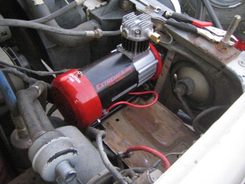1990 Ford Bronco - ExtremeAire air compressor with a finned cylinder head and red power cable, mounted on a tray in an engine bay.