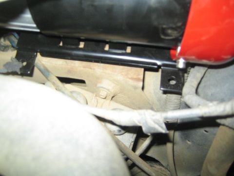 1990 Ford Bronco - black metal mounting bracket supporting a compressor, spanning over a hose and components beneath a vehicle.