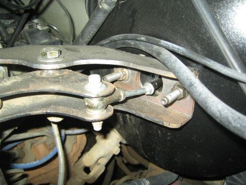 1990 Ford Bronco - adjustable threaded linkage and metal bracket bolted to a curved arm with hoses routed underneath a vehicle.