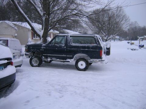 1994 Ford Bronco - A lifted Ford Bronco sits covered in snow on a residential street during winter.