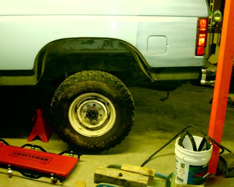 1985 Ford Bronco - The rear quarter panel, wheel, and bumper of a Ford Bronco are visible in this side view, which is supported by a jack stand.