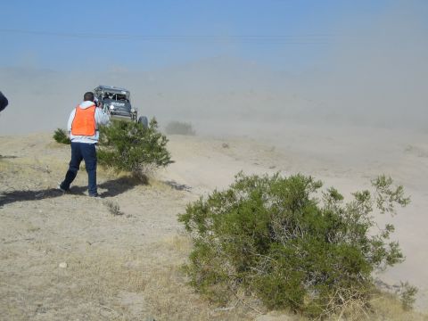 Man in orange vest photographing an off-road buggy raising dust in the desert