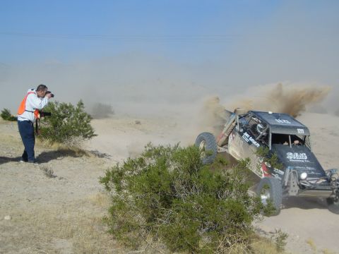 Off-road buggy throwing a rooster tail of dust while photographer in orange shoots