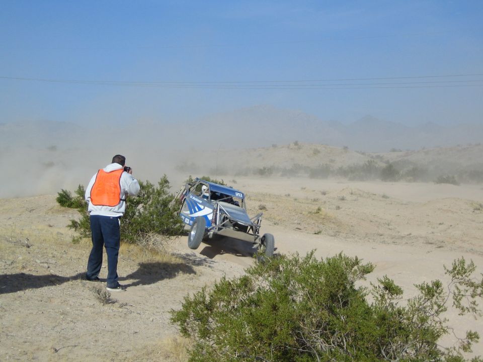 Blue tube-frame off-road buggy cresting a rise in the desert with photographer watching