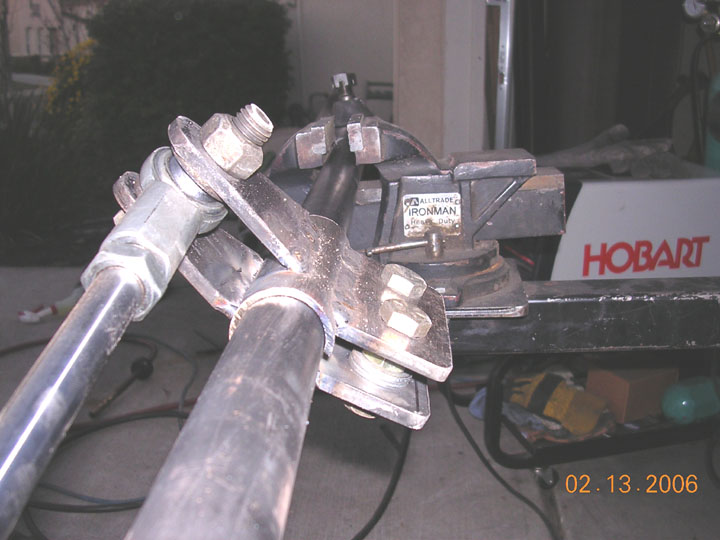 Fabricated link bracket with heim joints clamped in a bench vise beside a Hobart welder