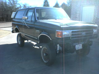 1991 Ford Bronco - A dark green 1991 Ford Bronco is shown with its suspension lifted and aftermarket wheels installed.