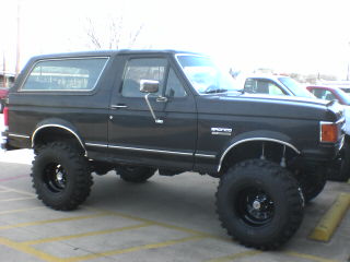 1991 Ford Bronco - This lifted 1991 Ford Bronco is shown from the front three-quarter angle, highlighting its substantial off-road tires.