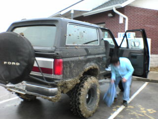 1991 Ford Bronco - A person is cleaning a muddy Ford Bronco parked in a lot with the rear door open.