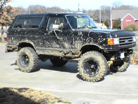 1991 Ford Bronco - Muddy 1991 Ford Bronco with aftermarket wheels and tires sits on a paved surface.