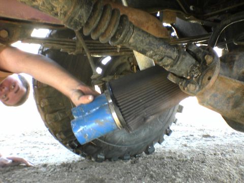 1991 Ford Bronco - A person is working on the undercarriage of a vehicle, holding an air filter near the drive shaft and tire.