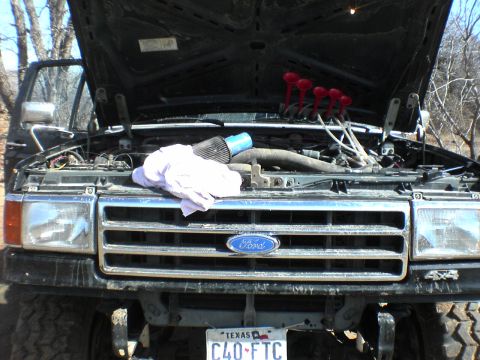 1991 Ford Bronco - The 1991 Ford Bronco's engine bay is visible with the hood up, revealing the Ford emblem and various engine components.