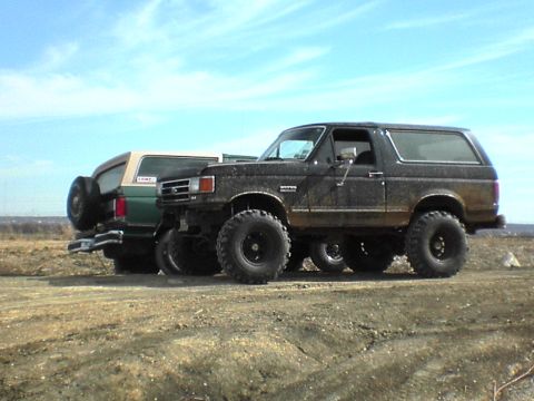 1991 Ford Bronco - Two Ford Broncos are parked on a dirt path under a blue sky.