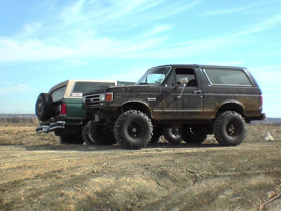 Two lifted Ford Broncos parked side-by-side on a dirt track