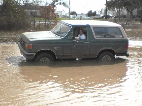1991 Ford Bronco - A 1991 Ford Bronco navigates through a flooded area, with its tires submerged in brown water.
