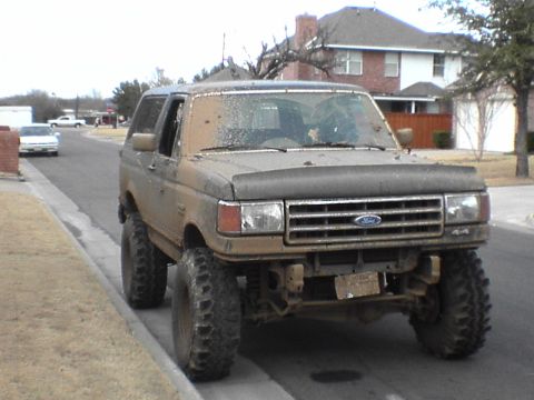 1991 Ford Bronco - Mud-covered 1991 Ford Bronco parked on the side of a residential street.