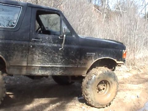 1991 Ford Bronco - A muddy black Ford Bronco with off-road tires navigates a dirt path.